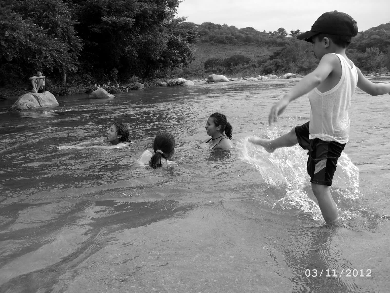 Johan as a boy, in a cap, kicking water in the river at El Coquillo while his family swims. 2012.