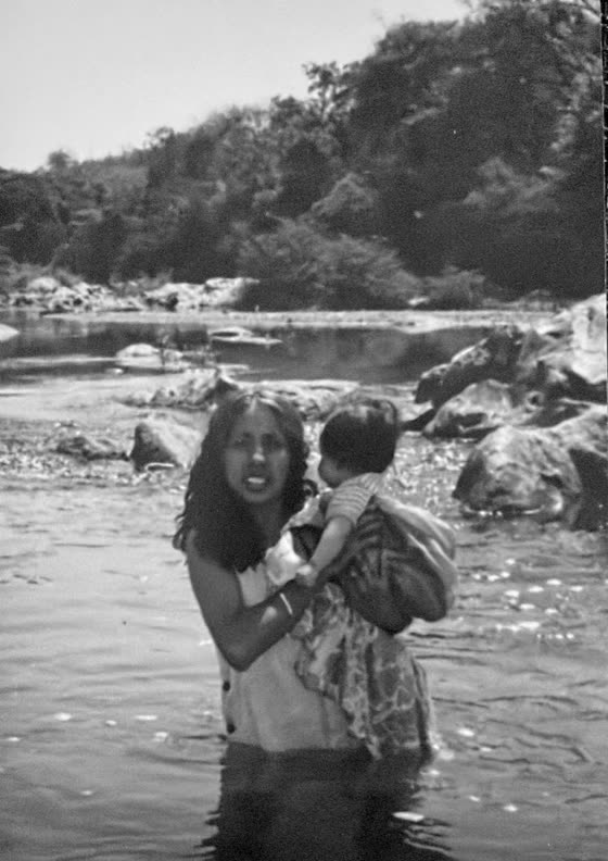 A woman carrying a baby across the river at El Coquillo