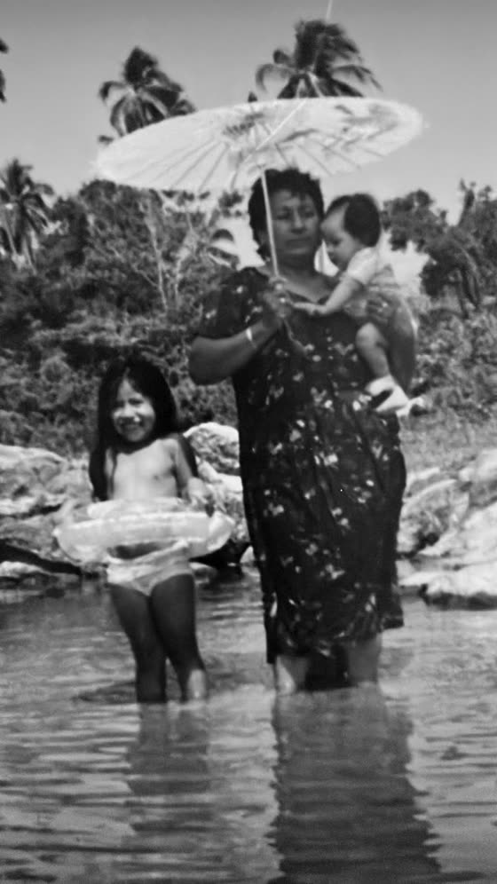 A woman with a paper parasol standing in the river with two children